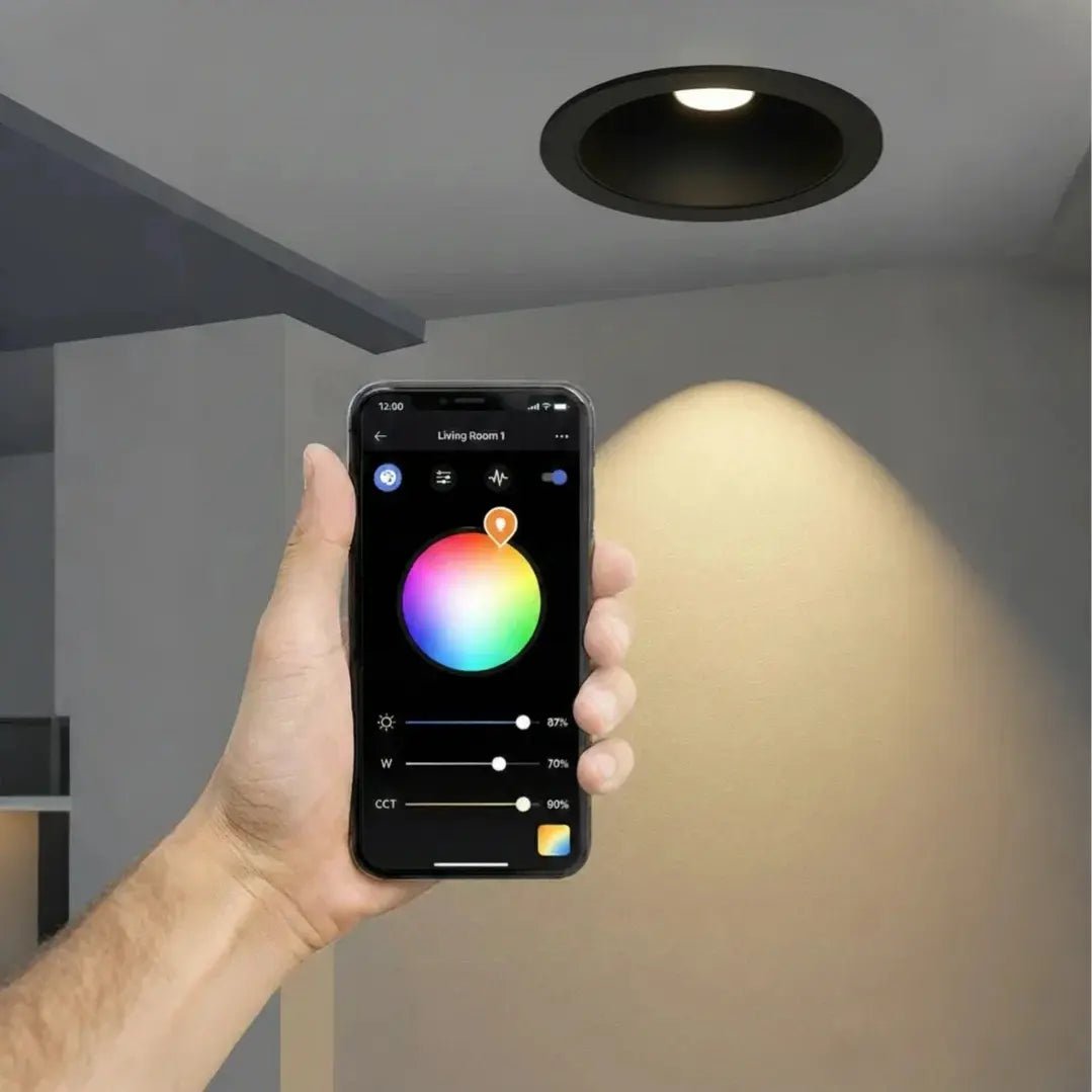 Hand holding a smartphone with a lighting control app next to a recessed ceiling light.