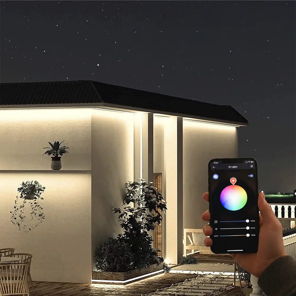 Hand holding a smartphone with a lighting app displayed, controlling outdoor lighting of a house.