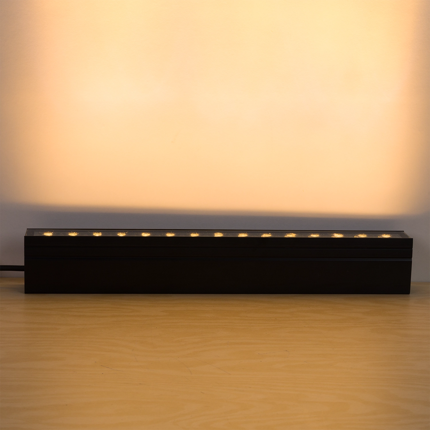 Long rectangular black light fixture on a wooden surface with a warm glow.