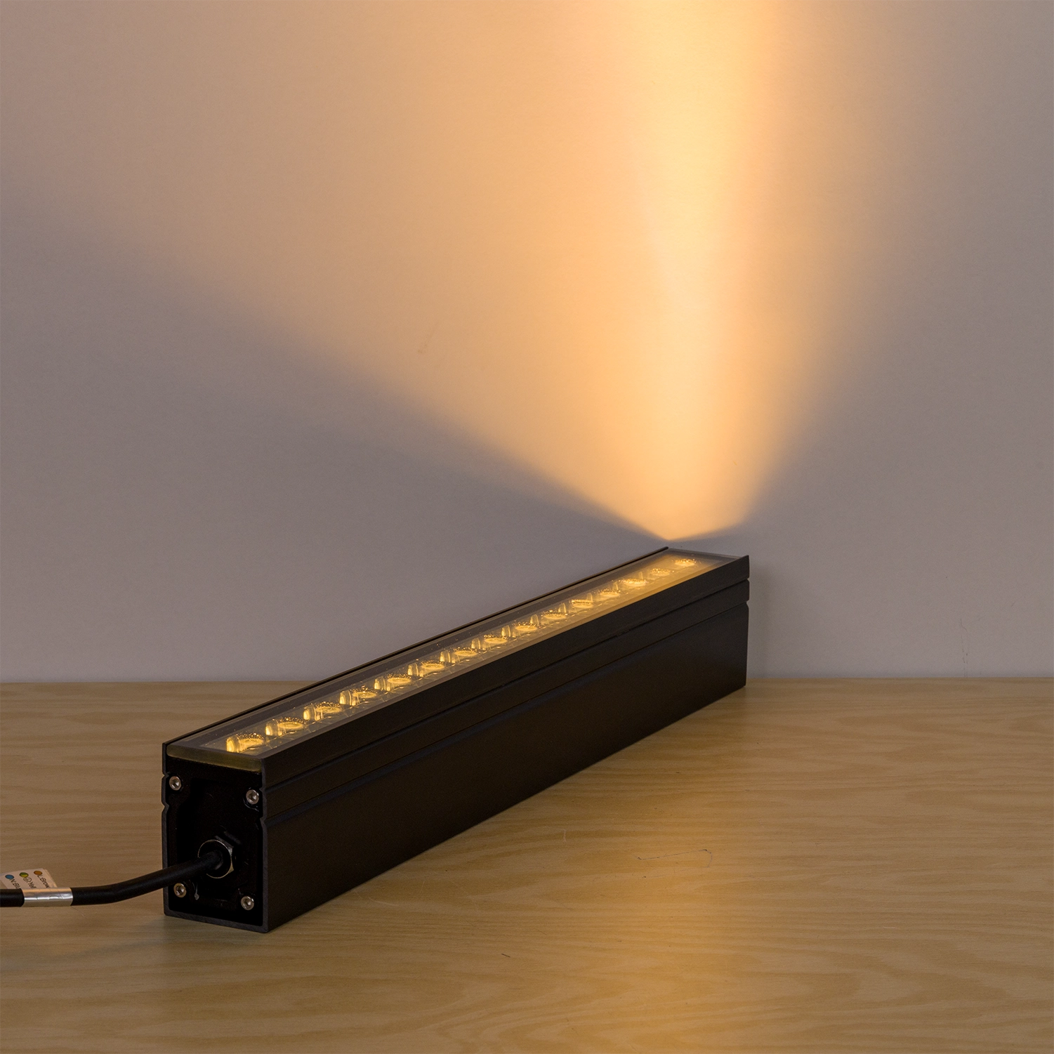 Long rectangular light fixture emitting a warm glow on a wooden surface with a neutral background