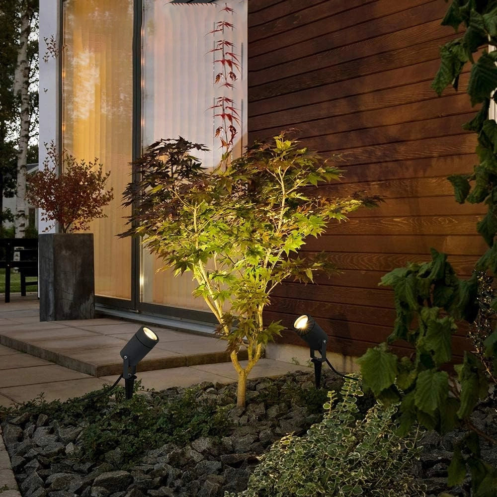 Outdoor garden scene with two black spotlights illuminating plants against a wooden wall.
