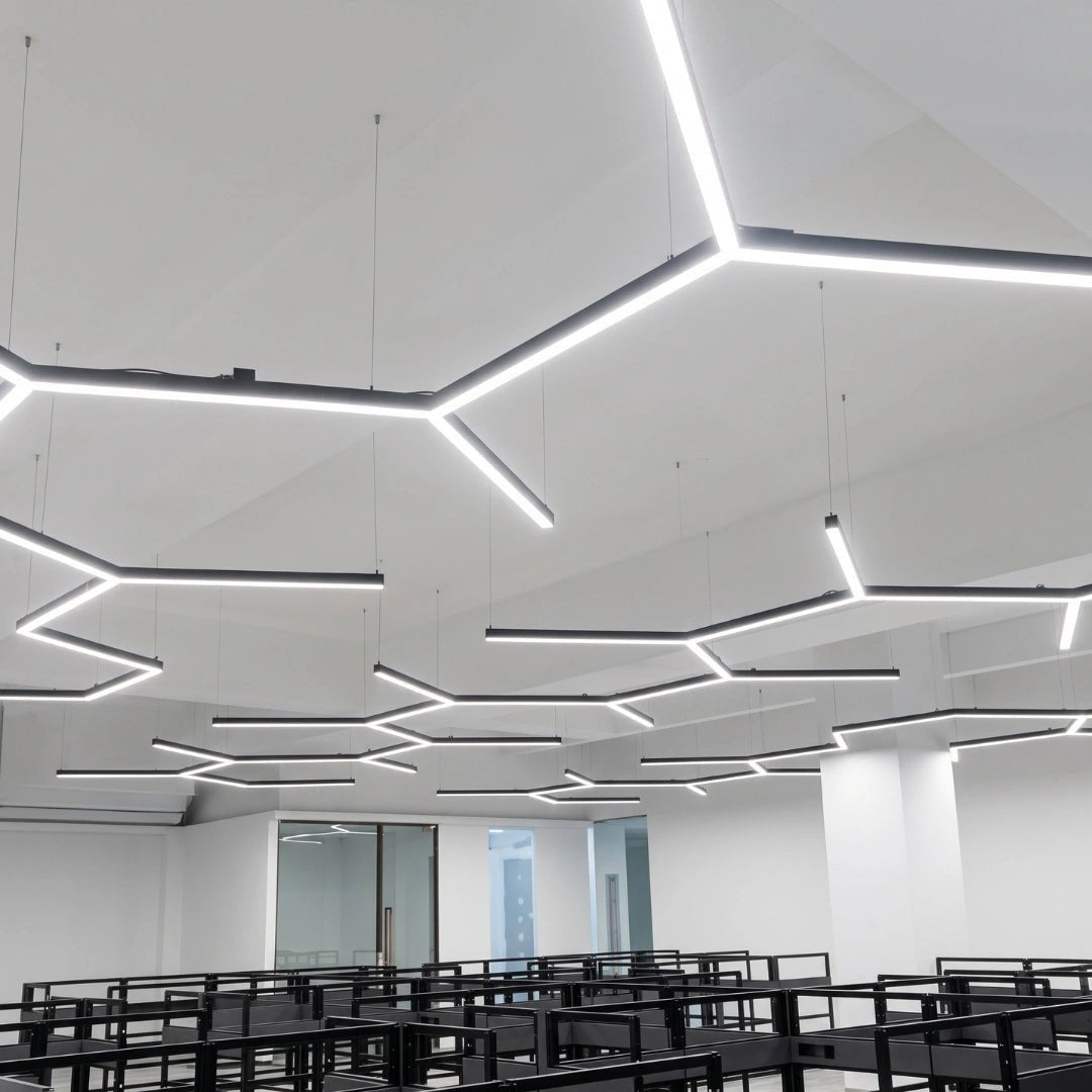 مصابيح سقف LED هندسية حديثة معلقة في فصل دراسي أو مكتب مشرق وبسيط التصميم، مع صفوف من المكاتب السوداء أسفلها.