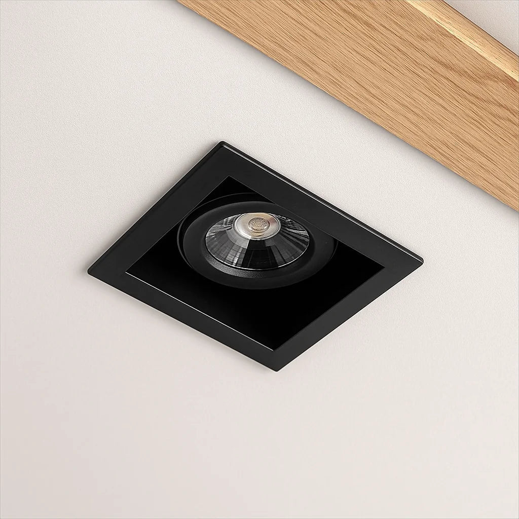 Black square recessed light fixture on a white ceiling with a wooden trim.