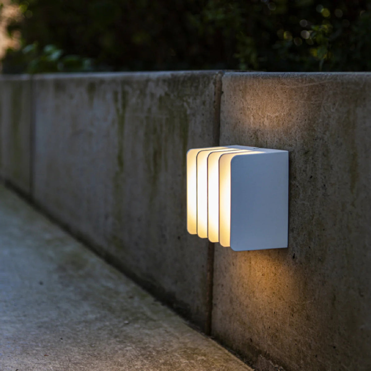 Modern outdoor wall light fixture on a concrete surface with a blurred natural background