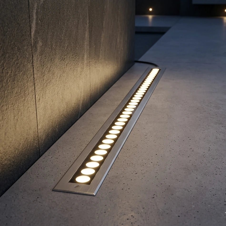 Linear outdoor light fixture on a concrete surface with a dark wall in the background