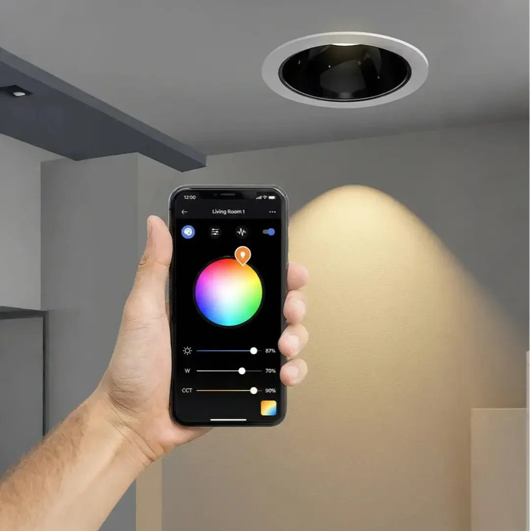 Hand holding a smartphone with a lighting control app, showing a smart light fixture on a ceiling.