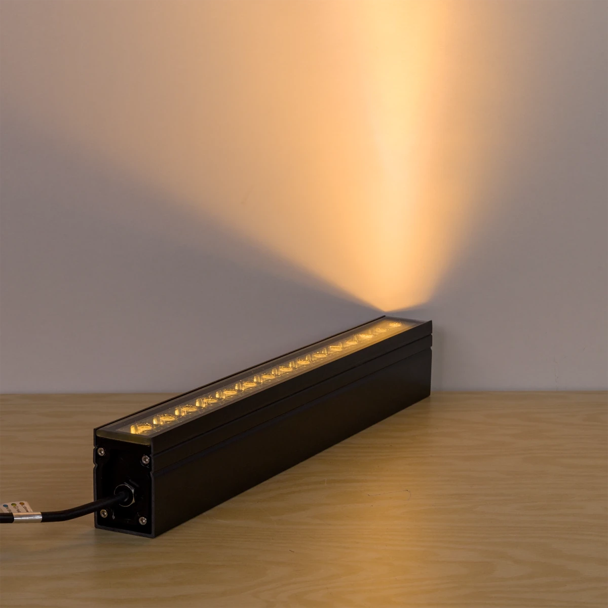 Long rectangular light fixture emitting a warm glow on a wooden surface with a neutral background