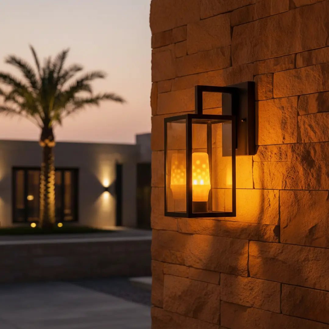 Decorative outdoor wall light fixture on a stone wall with palm trees and building in the background.
