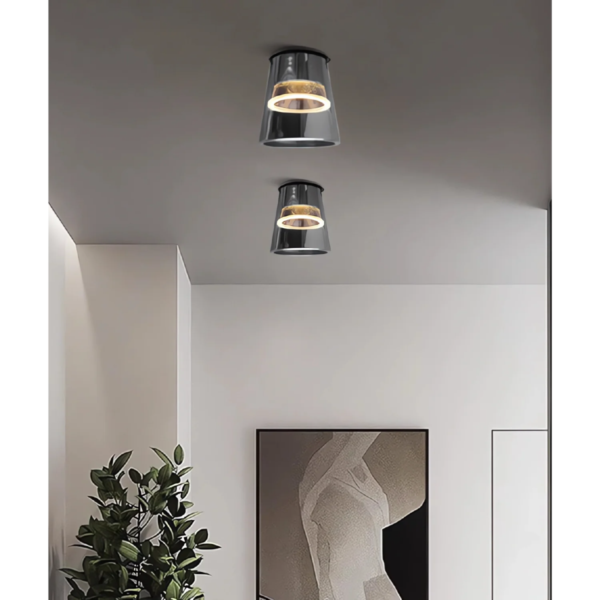 Two modern ceiling lights on a gray ceiling with a plant and abstract art in the foreground.