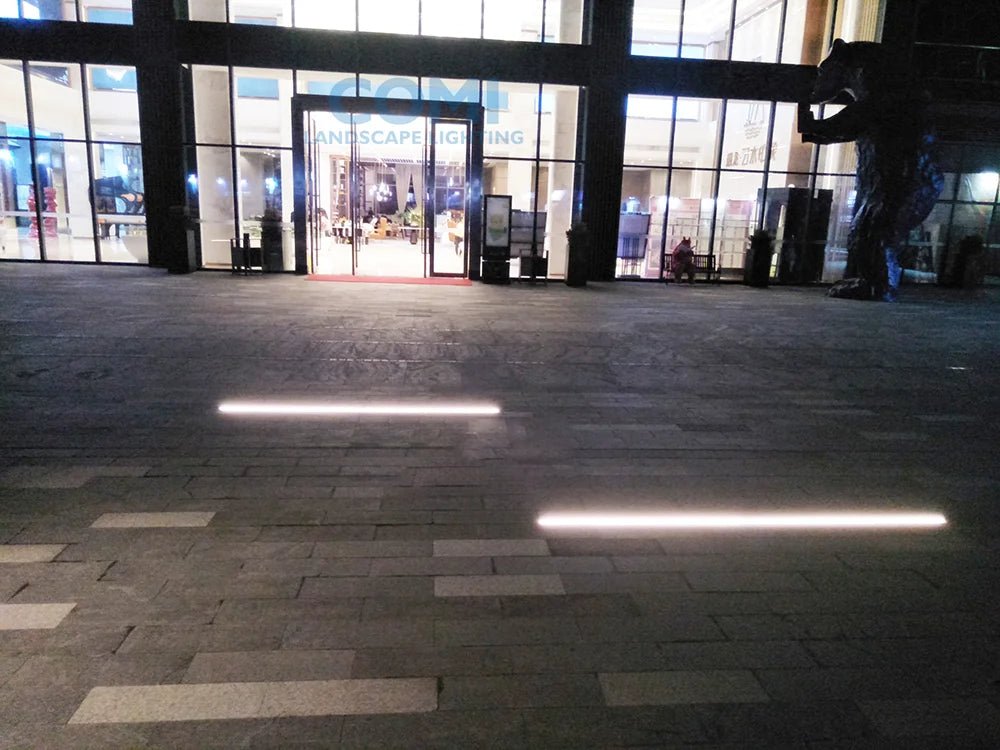 Large glass entrance to a building with people inside, illuminated by ceiling lights.