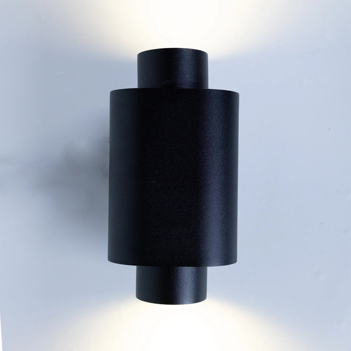 Black cylindrical wall light fixture on a gray background