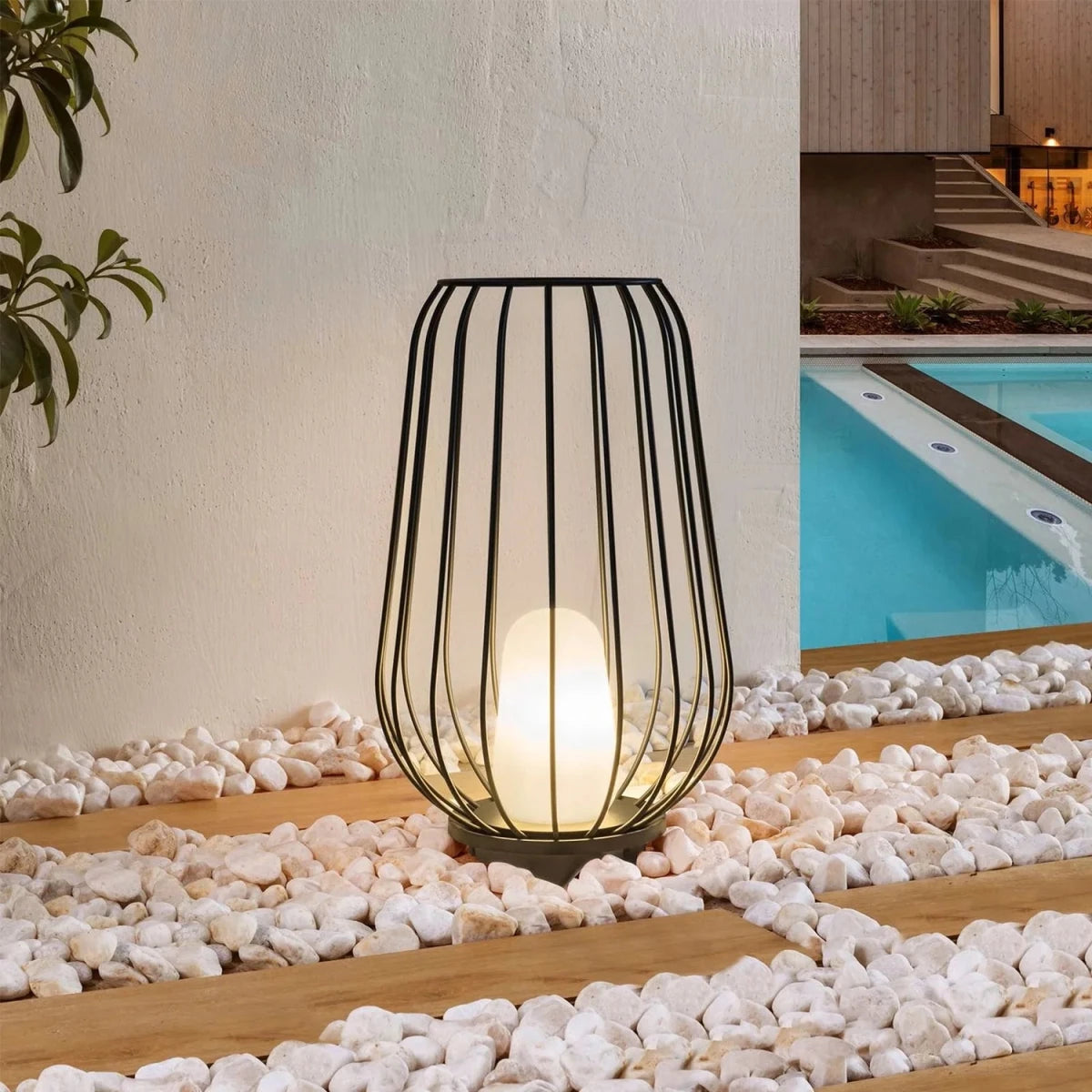 Decorative outdoor lamp with wire cage design on pebbles near a pool.