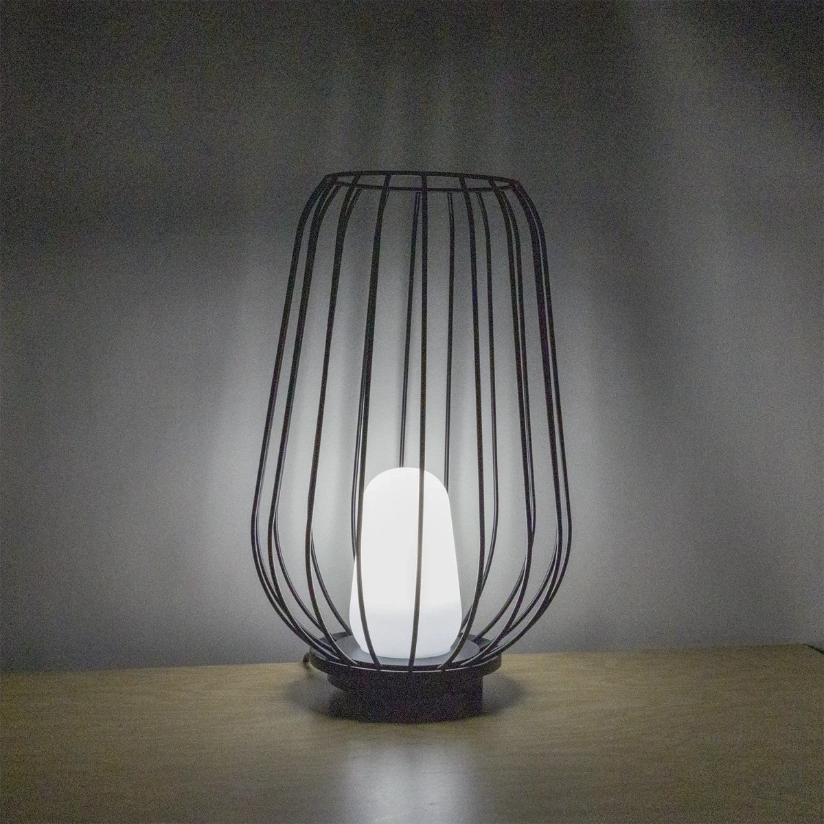 Black wire cage lamp with a white bulb on a wooden surface and gray background