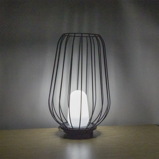 Black wire cage lamp with a white bulb on a wooden surface and gray background