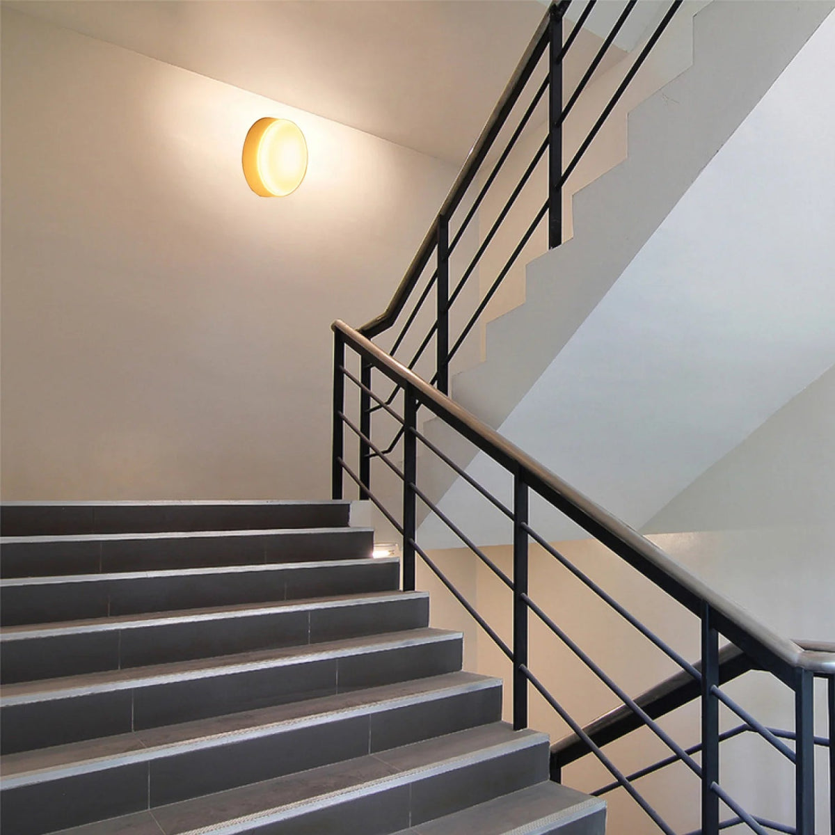 Staircase with black metal railing and a wall-mounted light fixture.