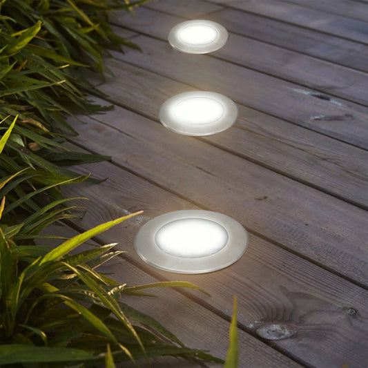 Three round white outdoor lights on a wooden deck with plants around.