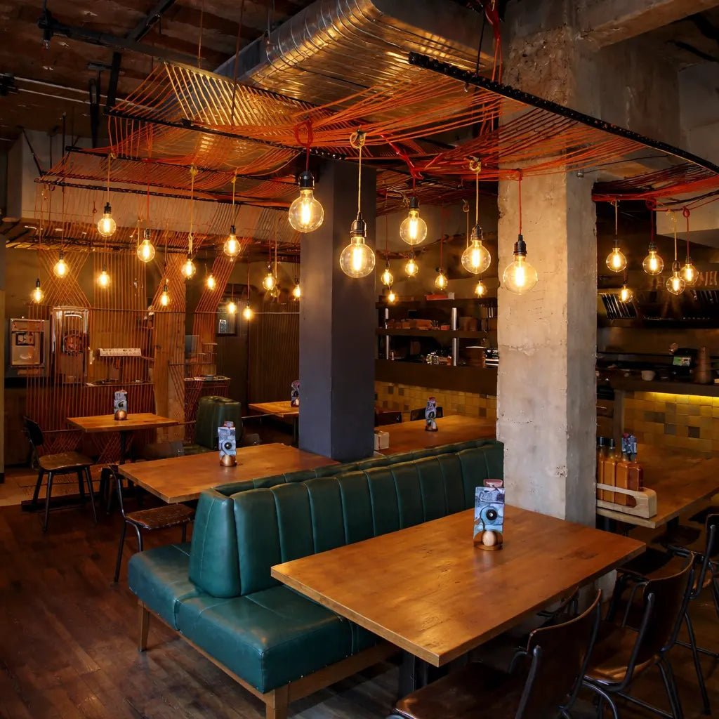 Modern restaurant interior with wooden tables, green booths, and exposed ceiling pipes.