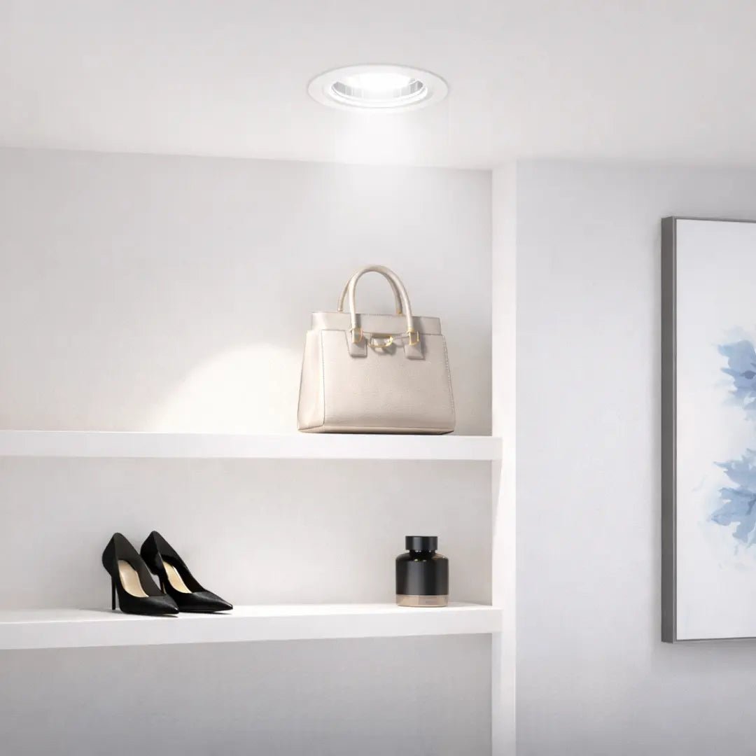 White handbag on a shelf with black high heels and a black vase against a white wall.
