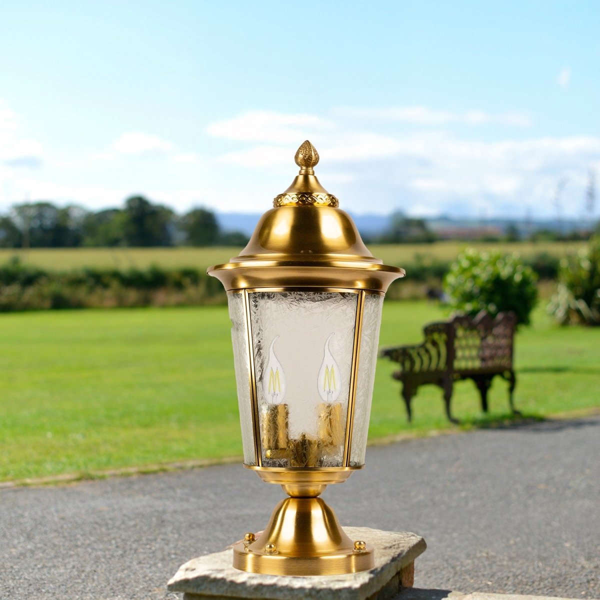 Gold outdoor lamp post with clear glass shade in a garden setting