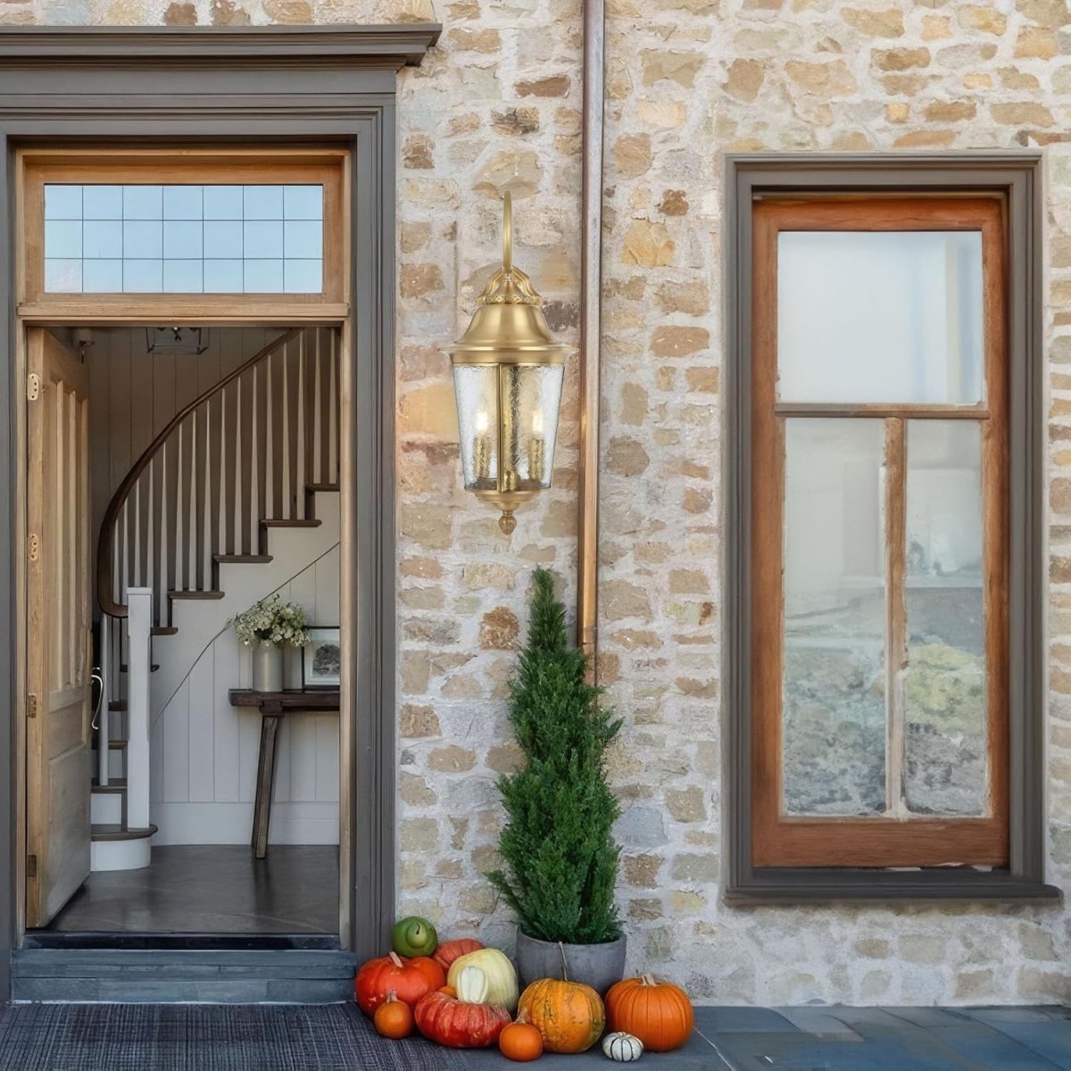 Front entrance of a house with stone wall, staircase, and decorative pumpkins on a rug.