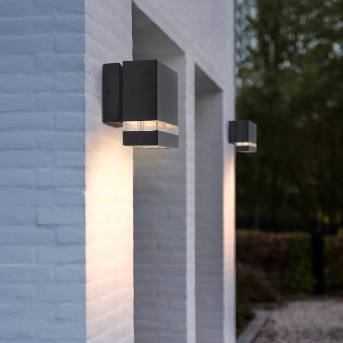 Modern outdoor wall lights on a brick wall with a blurred garden background