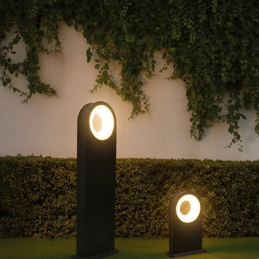 Two outdoor garden lights illuminated against a wall with greenery
