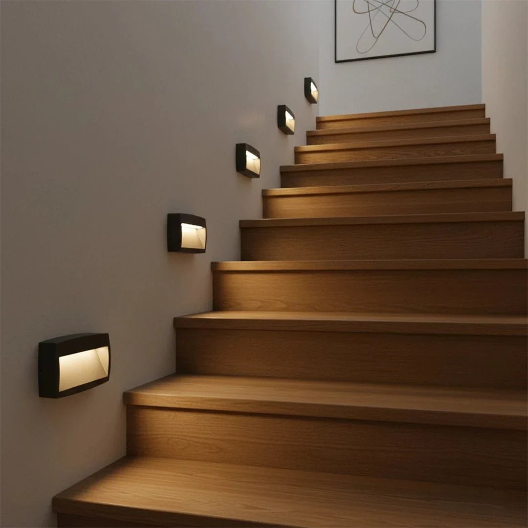 Wooden staircase with wall-mounted lights on a neutral wall.