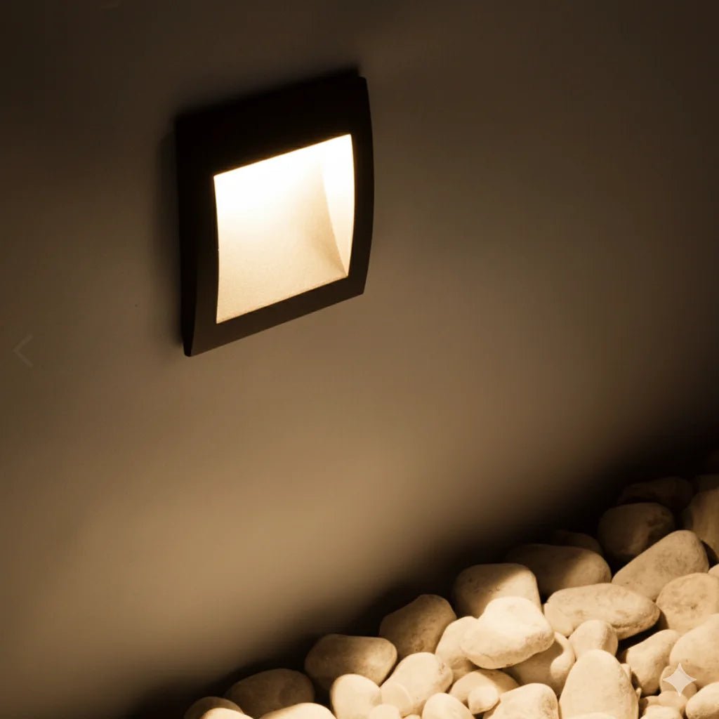 Square wall light fixture on a dark wall with pebbles at the base