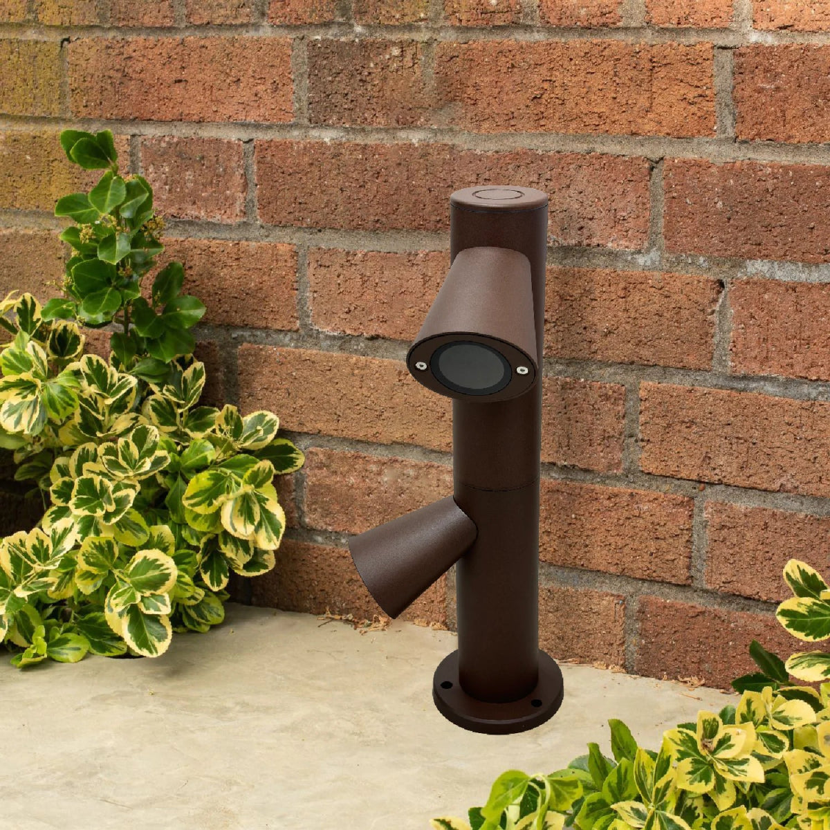 Brown outdoor light fixture on a stone surface with a brick wall and plants in the background