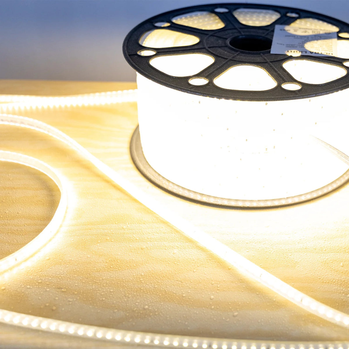 Spool of LED strip light with a warm glow on a reflective surface.