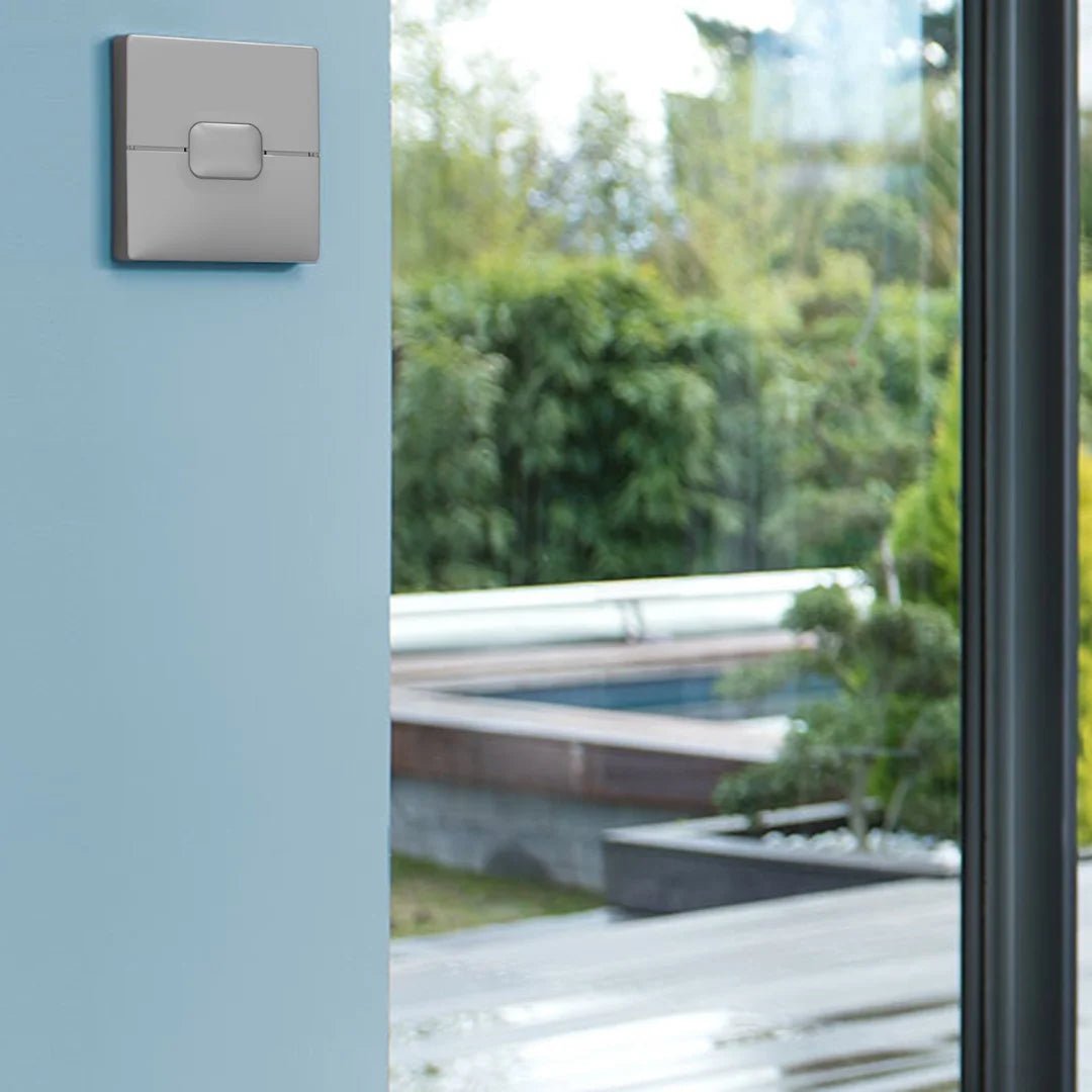 Modern light switch on a light blue wall with a view of greenery outside.