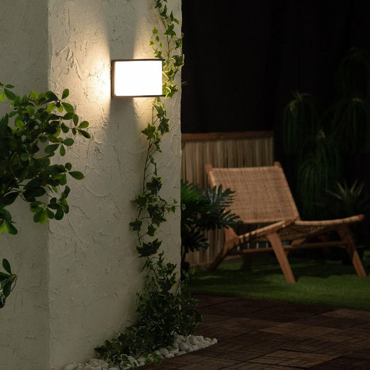 Outdoor setting with a wall-mounted light fixture, plants, and a wicker chair.